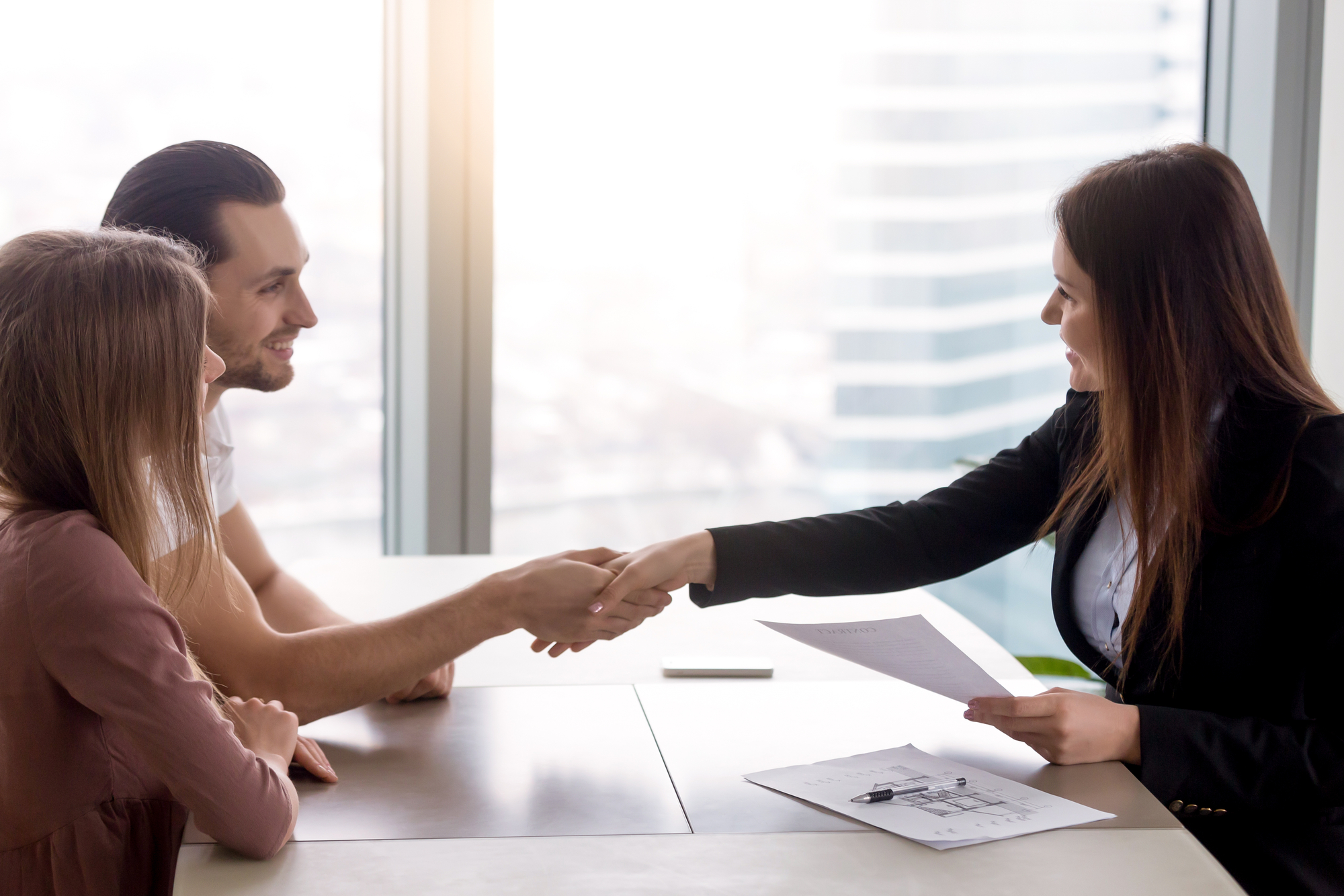 Young smiling couple visiting real estate agency shaking hands with realtor